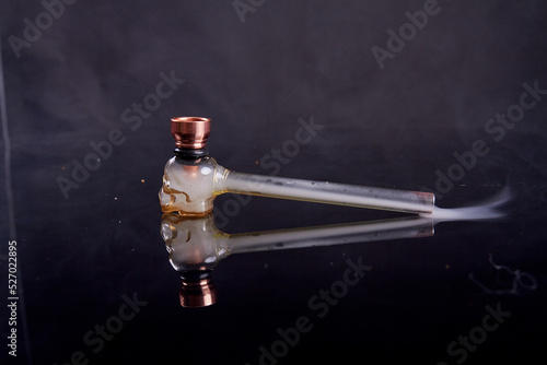 Glass pipe for crack or crystal meth on reflective mirror surface. Smoke on black background.