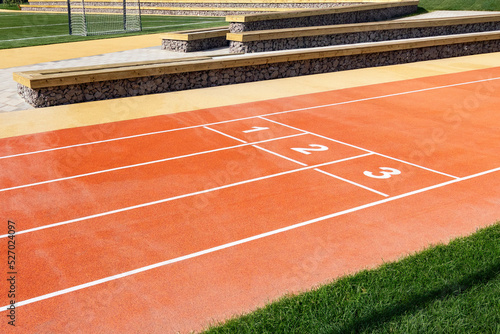 Sport stadium with red running tracks with numbers and green grass.