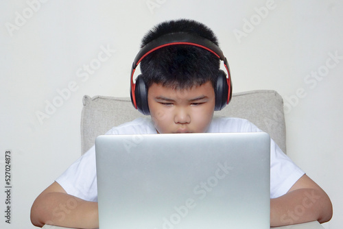 The boy sit on sofa is using laptop and wearing headphones. Education, learning and technology concept.