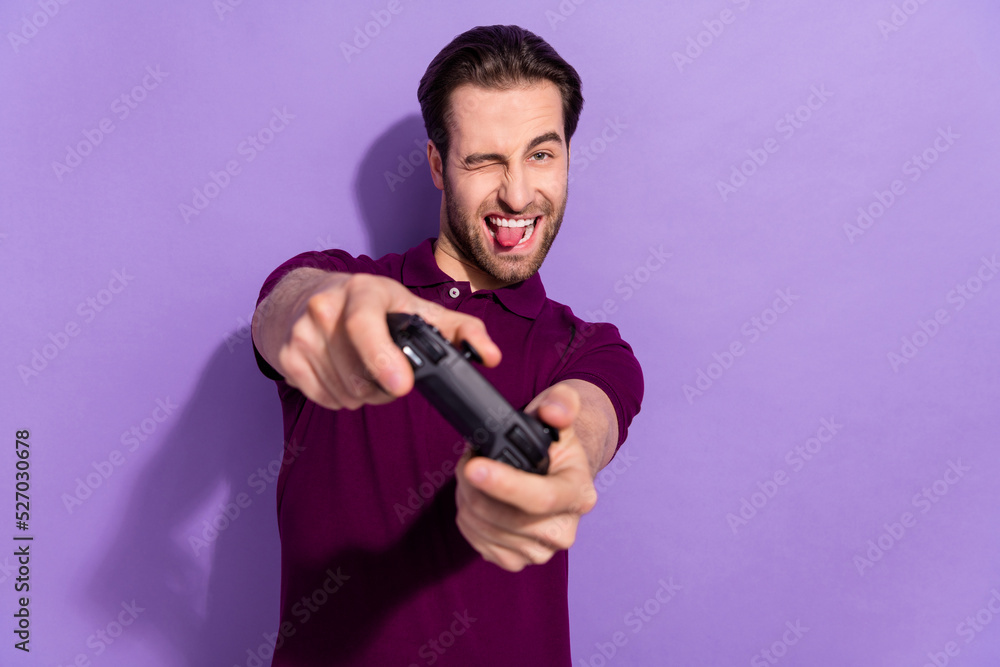 Photo of impressed millennial brunet guy play station tongue out wear violet t-shirt isolated on purple color background Photo of impressed millennial brunet guy play station tongue out wear violet t-shirt isolated on purple color background