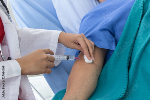 An Asian female doctor is making an injection in the shoulder of a patient in a hospital.