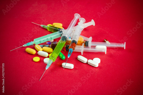 Pile of syringes and various colorful pills on red background. Drug addiction concept.