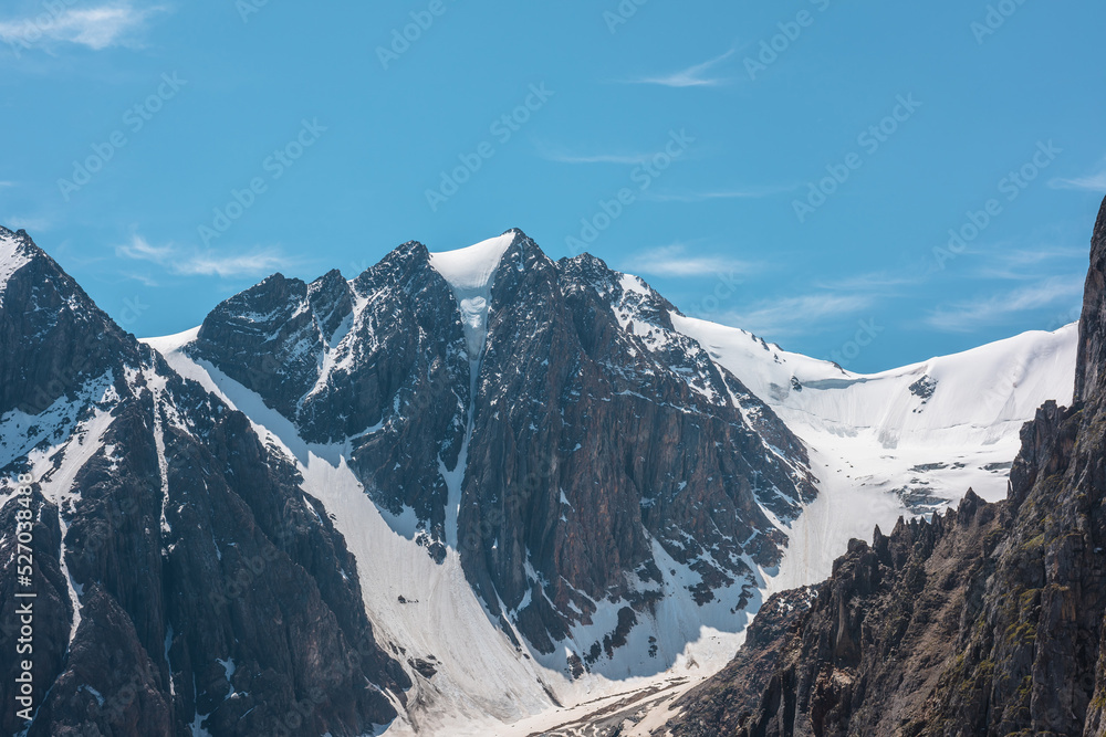 Scenic alpine landscape with snowy mountain peak in sunny day. Awesome landscape with rocky pinnacle with snow in sunlight. Beautiful view to snow mountain top and sharp rocks at very high altitude.