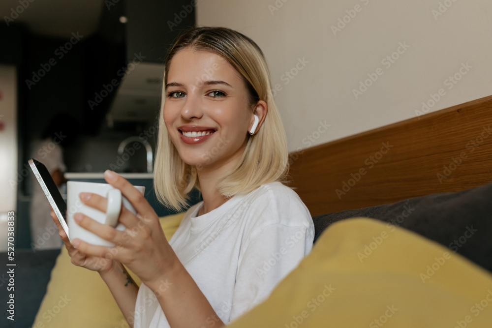 Close up portrait of charming smiling woman with wonderful smile posing at camera wearing white t-shirt is holding cup of coffee and smartphone . Close up portrait of charming smiling woman with wonderful smile posing at camera wearing white t-shirt is holding cup of coffee and smartphone .