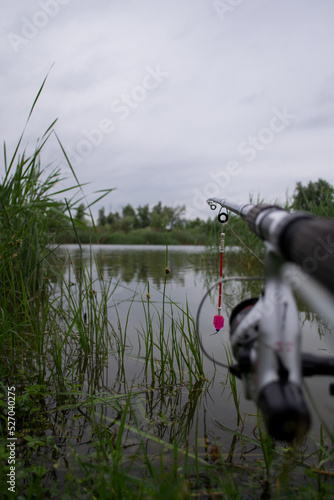A fishing rod equipped with a mechanical signal on the shore of the lake, waiting for a fish bite
