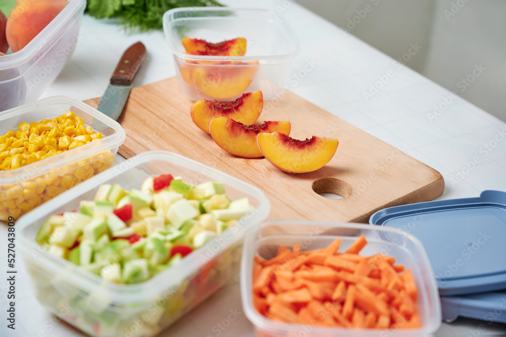 Fresh cut vegetables for freezing on table in kitchen. Slice of peaches and knife on cut board. Fresh cut vegetables for freezing on table in kitchen. Slice of peaches and knife on cut board.