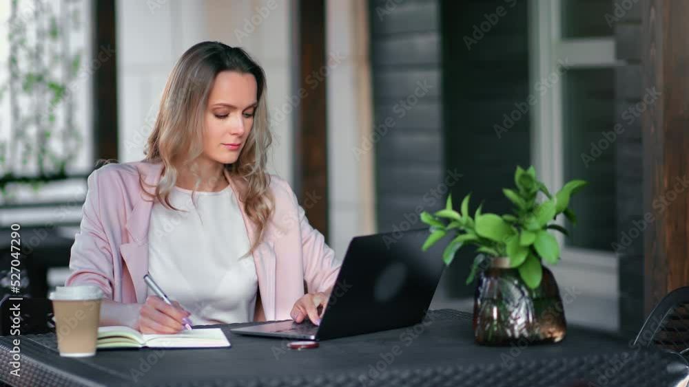 Focused business freelancer blonde woman working remotely at street cafe use laptop making notes Focused business freelancer blonde woman working remotely at street cafe use laptop making notes
