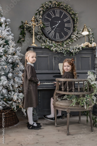 Two cute 5-6-year-old girls on a piano background in Christmas and New Year decorations. Retro style © Yelena Belodedova