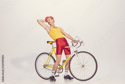 Portrait of young man in colorful clothes, uniform riding bike isolated over grey background. Looking relaxed. Chilling © Lustre
