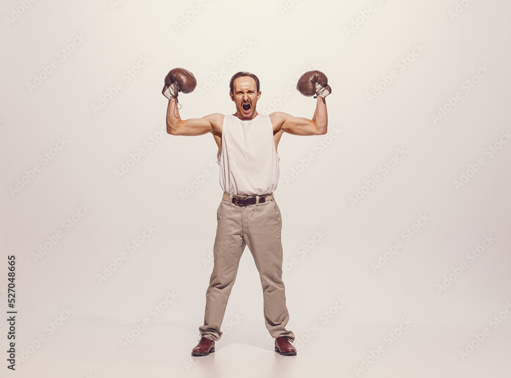 Portrait of muscular man in vintage clothes showing muscles in boxing gloves, posing isolated over grey studio background