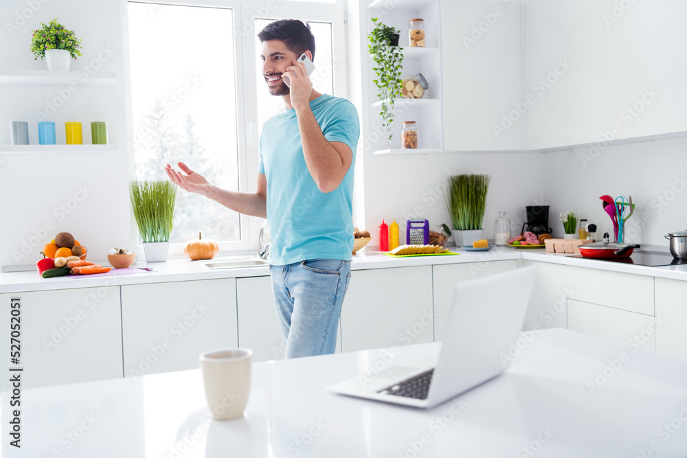Portrait of cheerful satisfied young man hold communicate telephone bright kitchen room indoors Portrait of cheerful satisfied young man hold communicate telephone bright kitchen room indoors