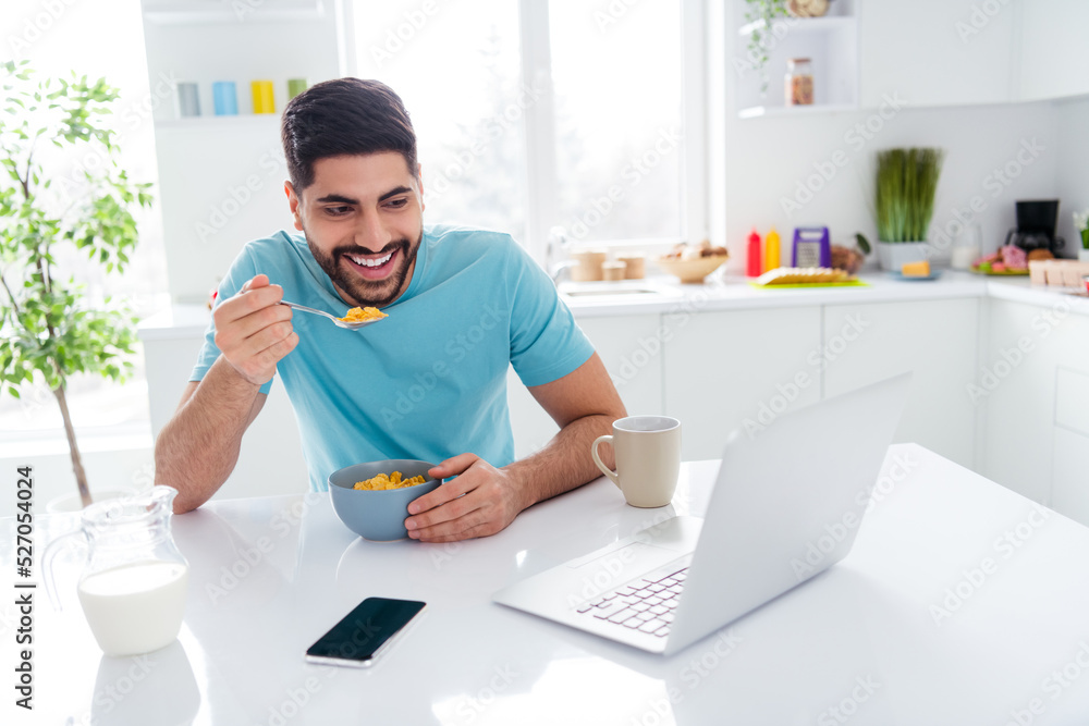 Photo of positive handsome guy hold spoon eat healthy cornflakes watch comedy video netbook free time morning indoors Photo of positive handsome guy hold spoon eat healthy cornflakes watch comedy video netbook free time morning indoors