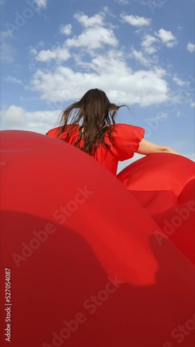 Slow motion of a girl in a red dress runs across a field with haystacks, the hem of her dress develops beautifully in the wind
