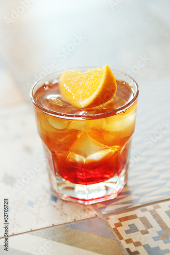lass of refreshing Negroni cocktail with bitter flavor and ice garnished with orange peel and served on marble table in room