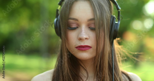 Pretty girl wearing headphones in outdoor park listening to music, song, podcast, or audiobook