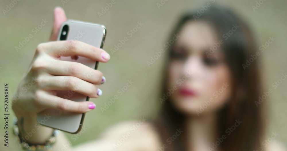 Pretty girl posing adjusting hair for selfie. Young woman holding smartphone taking photo of herself