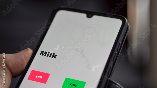 Un investisseur analyse le fonds ETF du lait à l'écran. Un téléphone montre les prix de l'ETF des matières premières alimentaires à investir, texte en anglais.