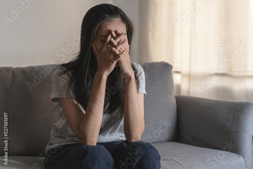 Asian woman covering her face feeling sorrow and depressed sit in the dark bedroom
