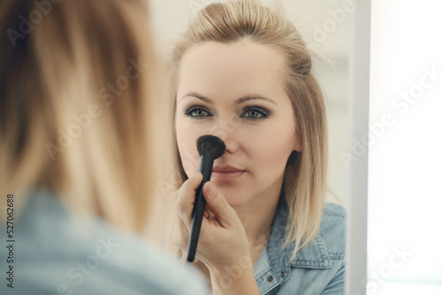 Blonde beautiful woman doing makeup in front of mirror