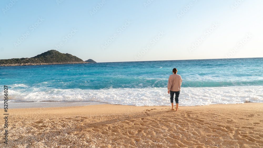 A woman walks along a deserted beach by the sea with waves