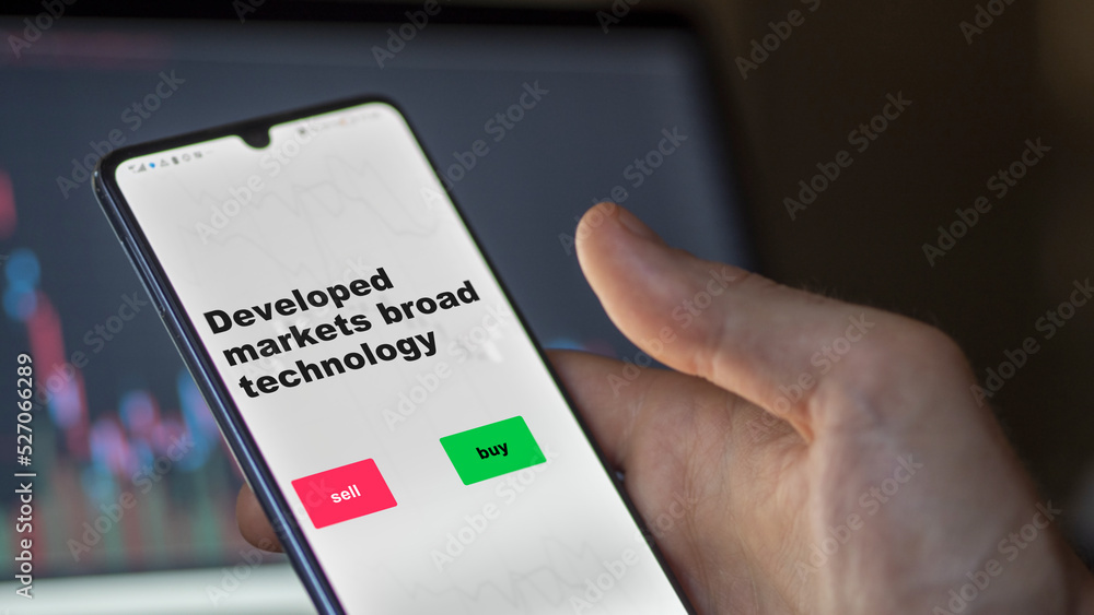 An investor's analyzing the stocks etf fund on screen. A phone shows the ETF's prices developed markets broad technology An investor's analyzing the stocks etf fund on screen. A phone shows the ETF's prices developed markets broad technology