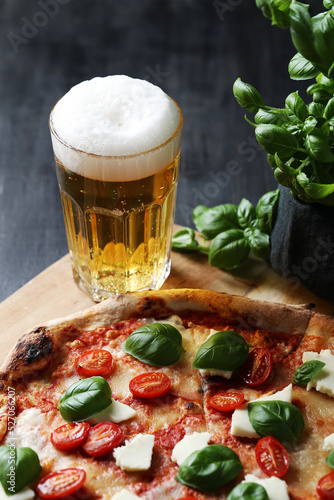 Whole tasty pizza with cheese, cherry tomatoes and glass of cold beer on a wooden board