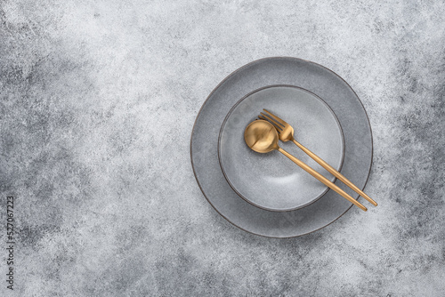 Gray ceramic plates with golden cutlery. Gray stone grunge background. Minimal table setting. View from above