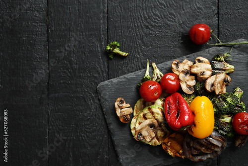 Picture of tasty hot grilled food with various vegeables on a black wooden cutting board