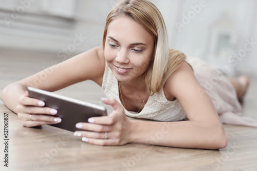 A picture of a beautiful young woman using a digital tablet and lying on the floor
