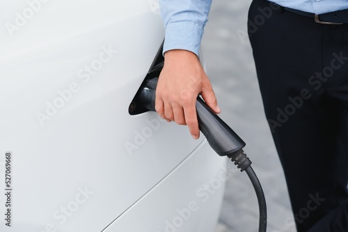 a businessman charges an electric car. © Serhii