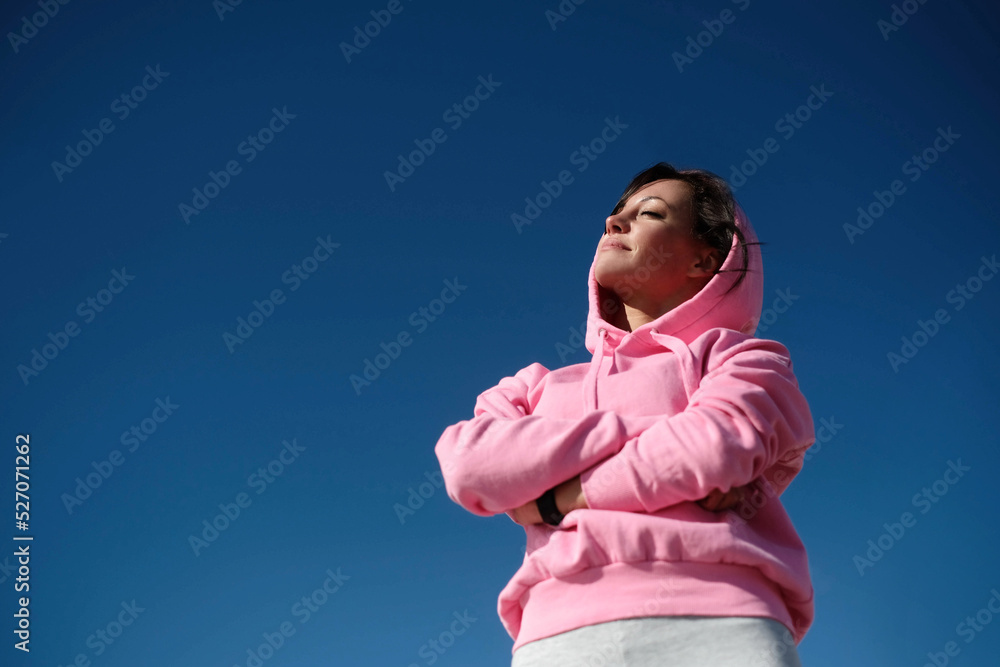 A beautiful young woman in pink sports clothes with a hood posing with crossed arms A beautiful young woman in pink sports clothes with a hood posing with crossed arms