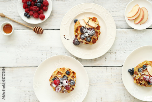 Top view of Belgian waffles with berries and powdered sugar on a wooden surface.