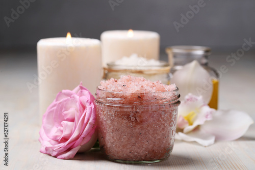 A glass jar of pink sea salt and two candles for cosmetologic procedures