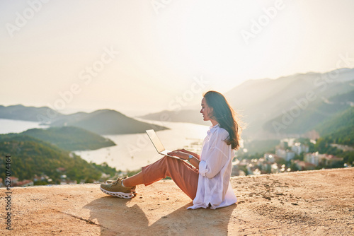 Free happy inspired freelancer girl enjoys remote works at a computer at sunset with beautiful view. Online working everywhere photo