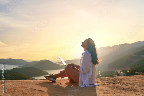 Papier peint Free happy inspired freelancer girl enjoys remote works at a computer at sunset with beautiful view