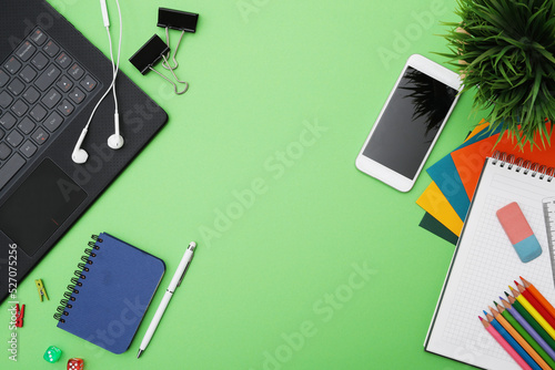 Top view of different stationeries with computer and mobile phone isolated on a green background