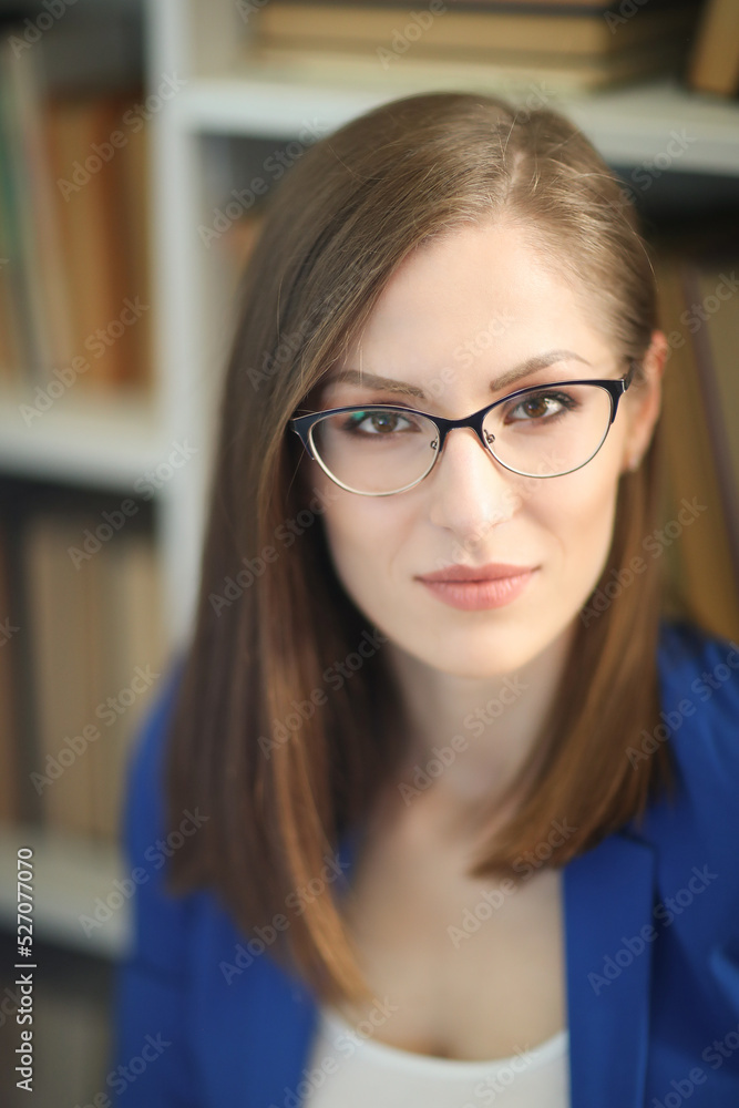 Close-up portrait of a beautiful, attractive girl in a blue jacket and a white t-shirt,in glasses against bookshelf background Close-up portrait of a beautiful, attractive girl in a blue jacket and a white t-shirt,in glasses against bookshelf background