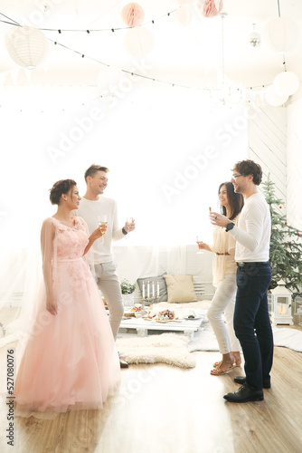 A group of young people standing with glasses of champagne and talking to each other at a party