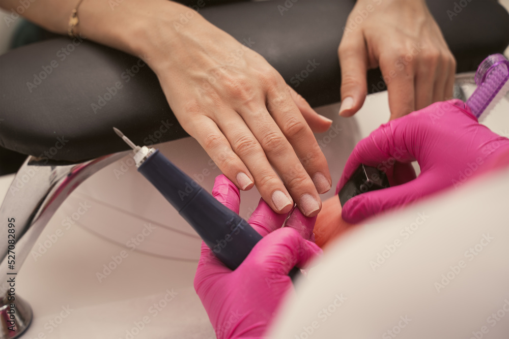 Manicure salon master removes nail polish uses an electric nail file. Woman getting nail manicure. Professional manicure in beauty salon. Hygiene and care for hands. Beauty industry concept