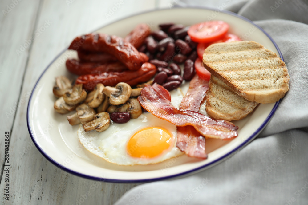 Close view of English breakfast with fried eggs, bacon,sausages, bread and vegetables in white plate. Close view of English breakfast with fried eggs, bacon,sausages, bread and vegetables in white plate.