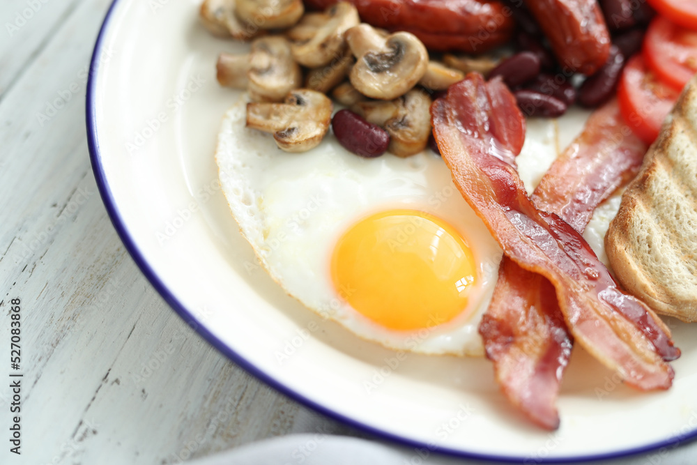 Close view of English breakfast with fried eggs, bacon,sausages, bread and vegetables in white plate. Close view of English breakfast with fried eggs, bacon,sausages, bread and vegetables in white plate.