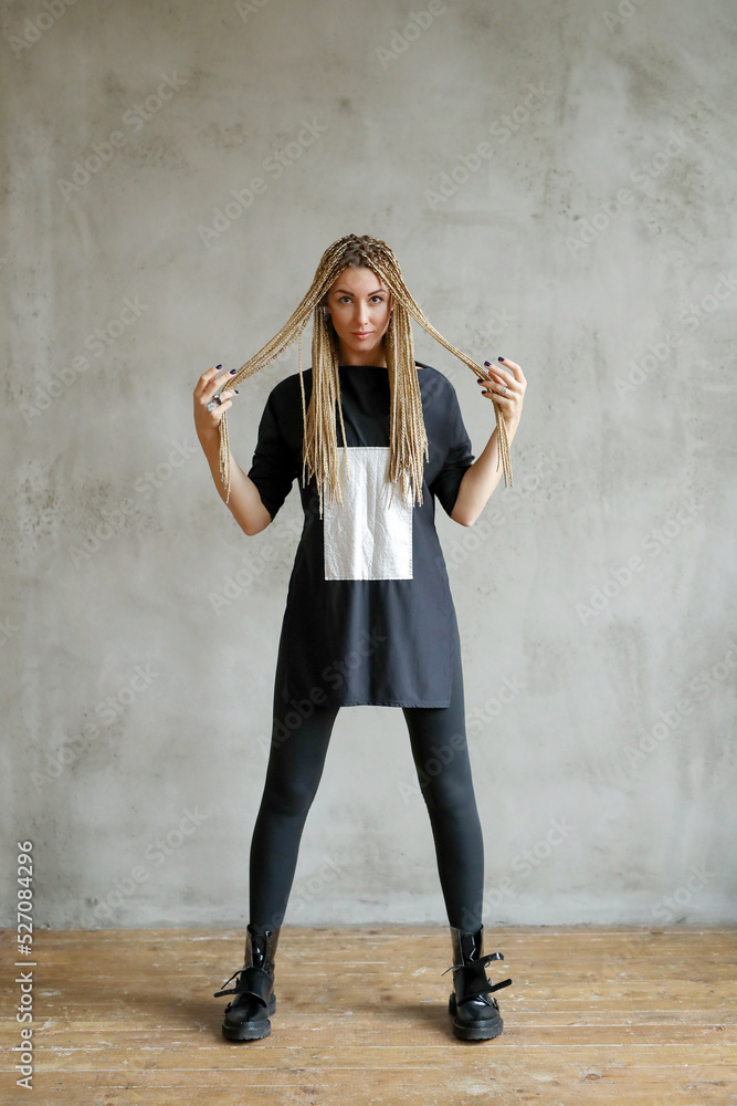 Fototapeta premium Full-size photo of a young woman with dreadlocks wearing oversize shirt standing and posing against stone background.
