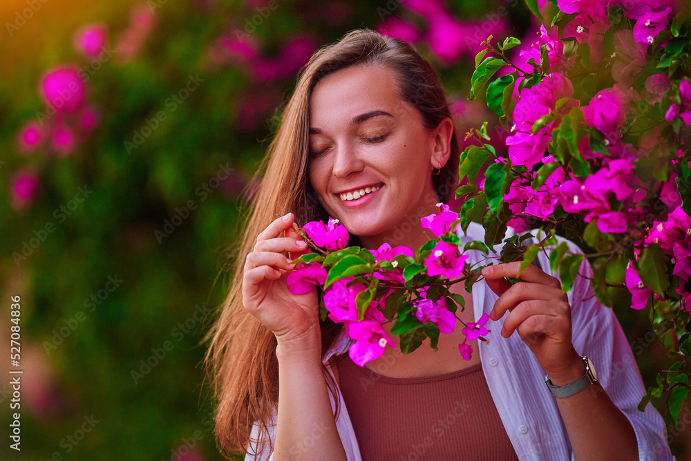 Fototapeta premium Portrait of a happy cute smiling caucasian girl with closed eyes and a branch of pink flowers in the garden outdoors