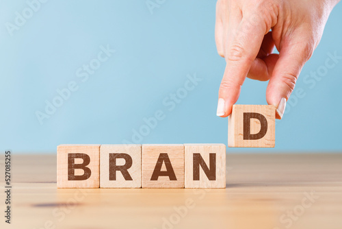 Woman hand putting wood cube block with word Brand on wooden table. Brand building for success concept
