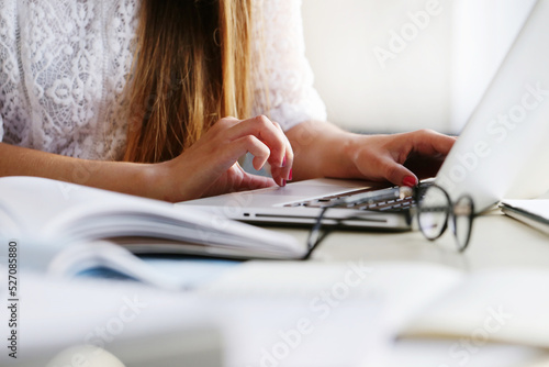 Beautiful, sweet, young girl with long hair sitting and working on the computer against windowsill.