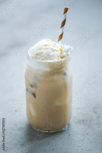 A glass cup of iced coffee with whipped cream on top and straw 