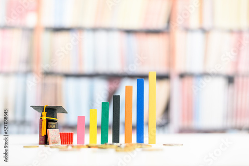 Education and life long learning is the key success, educational concept : Black graduation cap or a mortarboard, textbooks, increasing height color bar graphs with blurred bookshelf background.