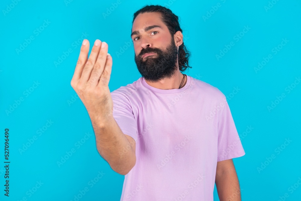 young bearded man wearing violet T-shirt over blue studio background Doing Italian gesture with hand and fingers confident expression young bearded man wearing violet T-shirt over blue studio background Doing Italian gesture with hand and fingers confident expression