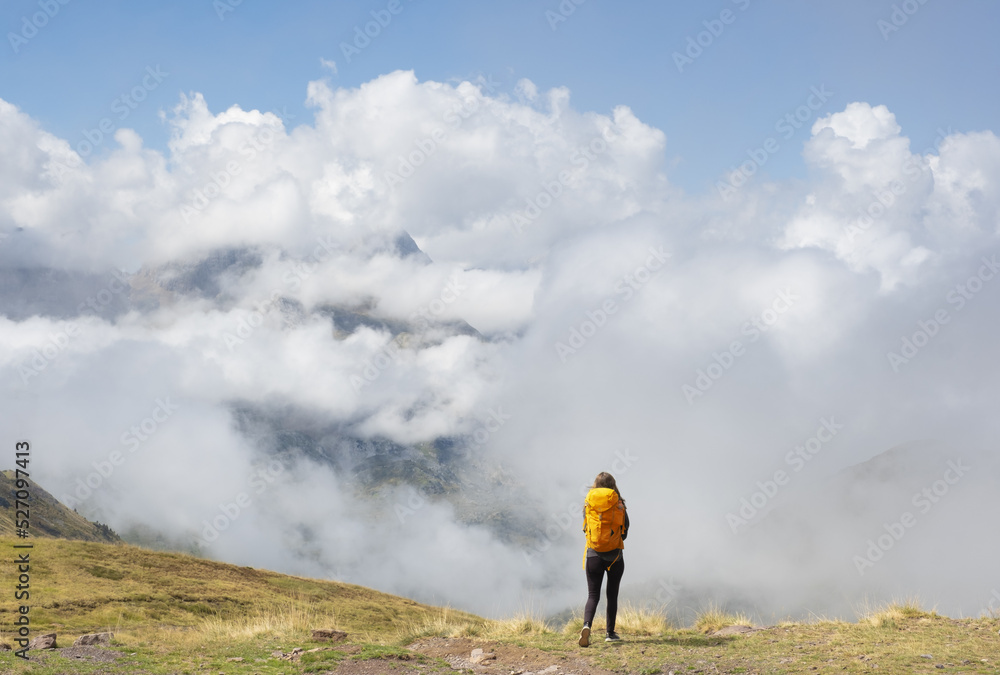 Girl with yellow backpack hiking in the Pyrenees, with the mountains in the clouds in the background.