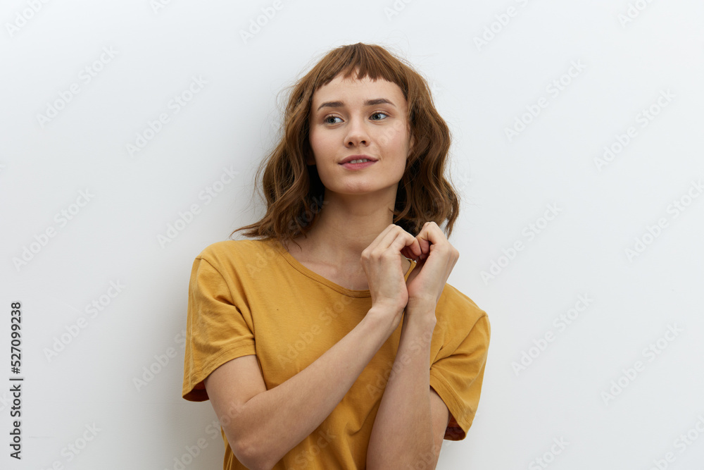 attractive, redhead, romantic a woman standing in a yellow T-shirt on a white background and shows a heart sign with her fingers, smiling broadly and looking away. Horizontal photo with empty space attractive, redhead, romantic a woman standing in a yellow T-shirt on a white background and shows a heart sign with her fingers, smiling broadly and looking away. Horizontal photo with empty space